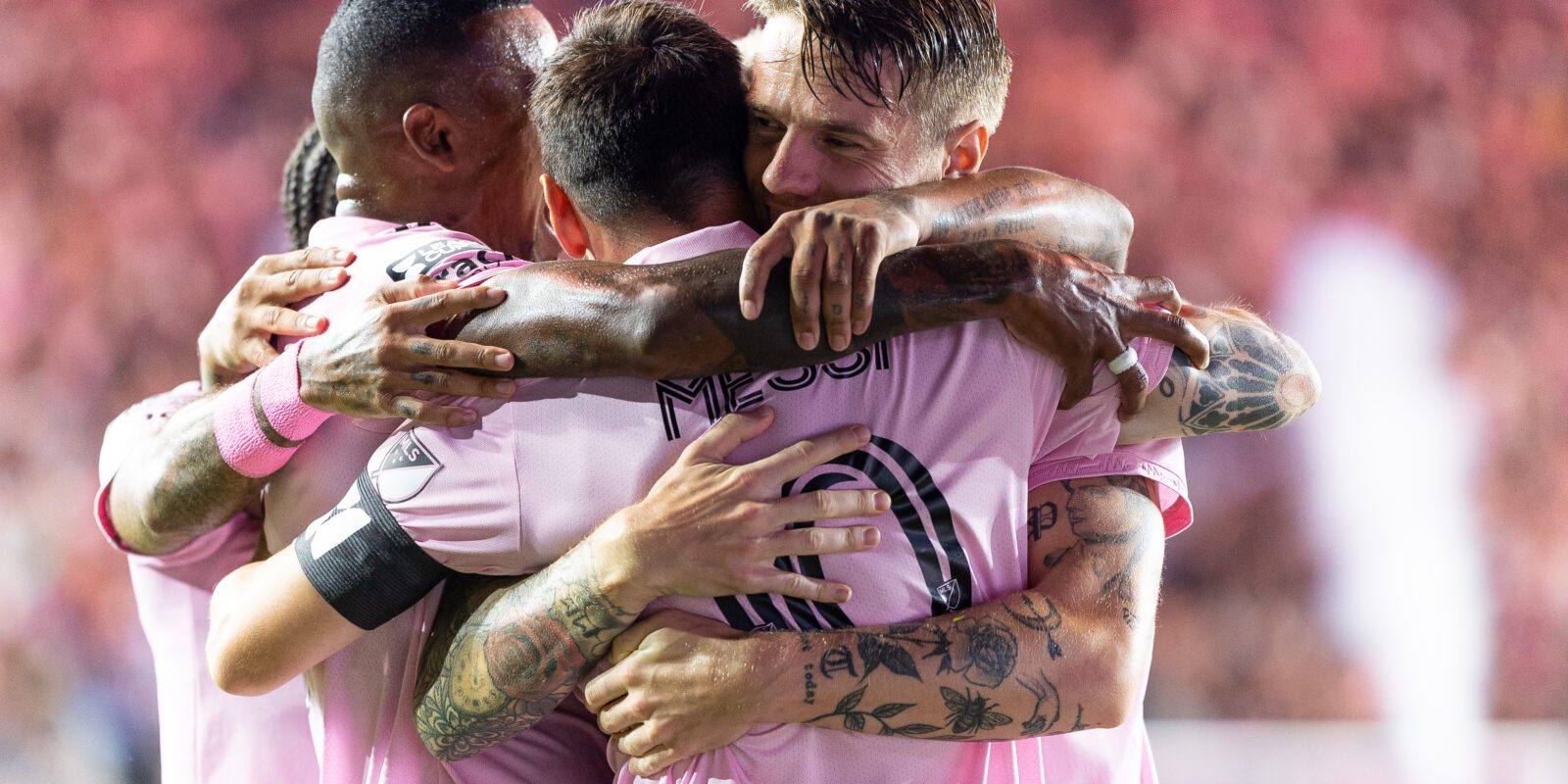 A group of Inter Miami football players including Lionel Messi are hugging and celebrating